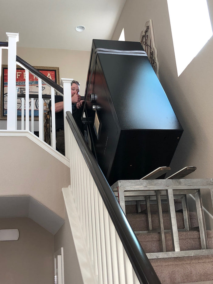A safe strapped to a stair-climbing dolly being navigated up an interior staircase