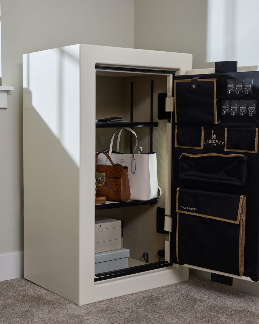 An open home safe in a bedroom holding handbags, a jewelry box, and documents on the door organizer