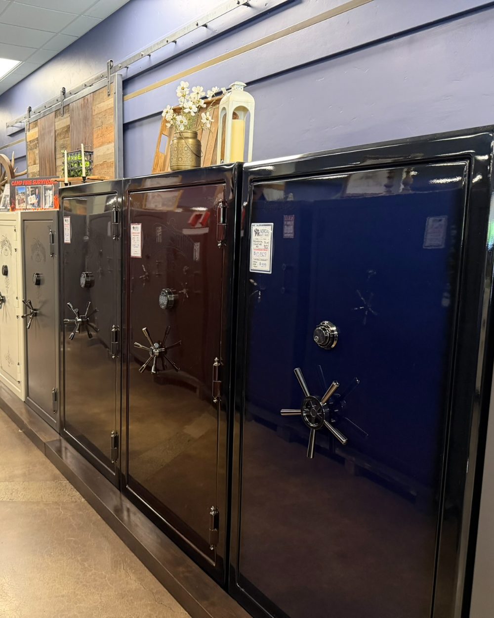 A row of safes in the Norcal Safe and Vault showroom, from cream and gray gun safes to a black and a deep blue high-gloss safe, showing the range of safe categories