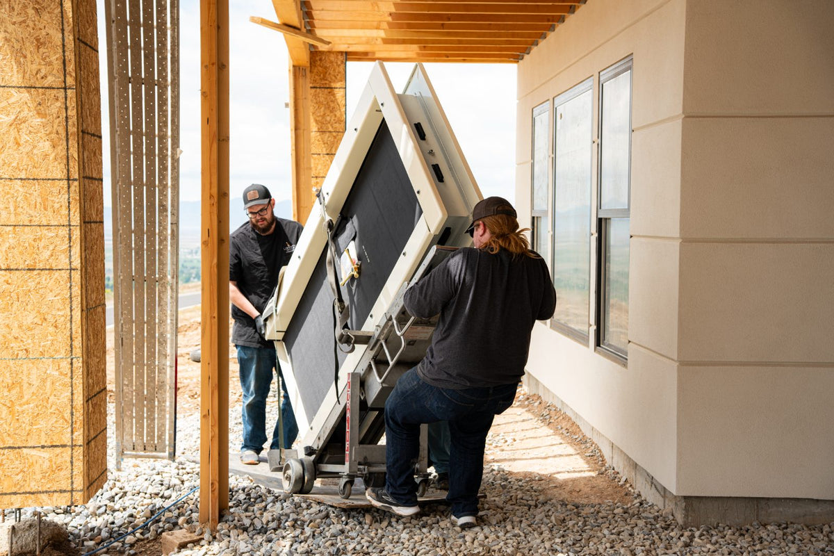 Two Norcal Safe and Vault installers maneuvering a vault door on a specialty lift dolly into a home under construction, mountains visible in the background