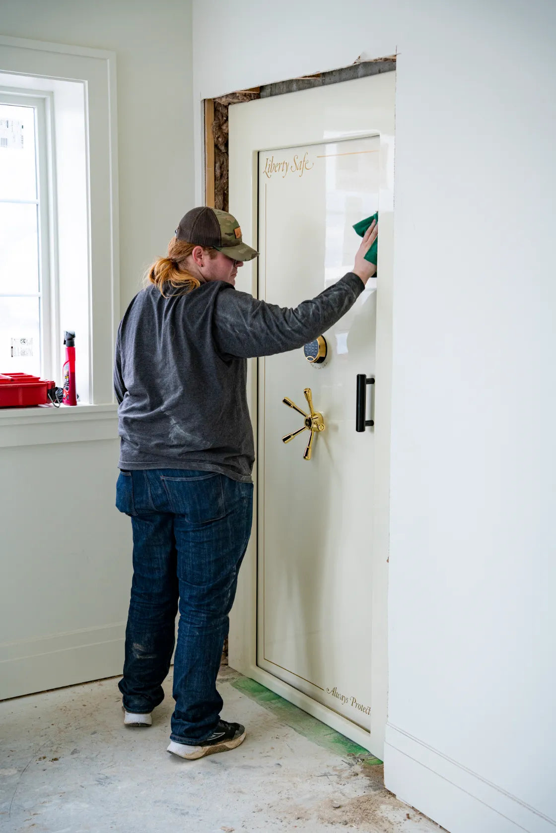 A Norcal installer finishing a cream Liberty vault door set into a reinforced opening mid-construction, with the wall framing still exposed